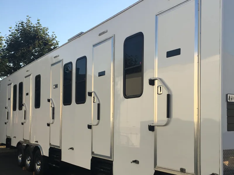 A white multi-room honeywagon trailer with triple axles, four separate doors and diamond-plate fenders.