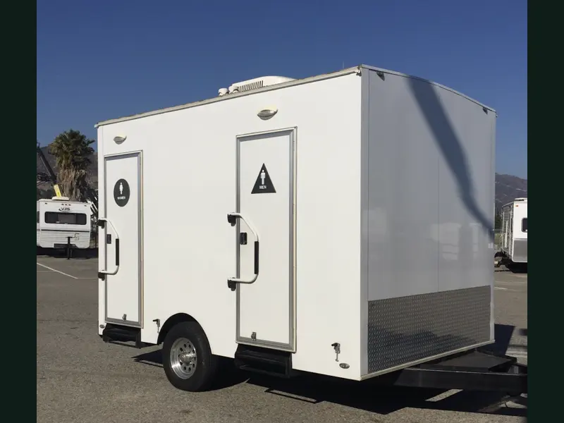 A white restroom trailer with separate men and women entrances, parked on asphalt.
