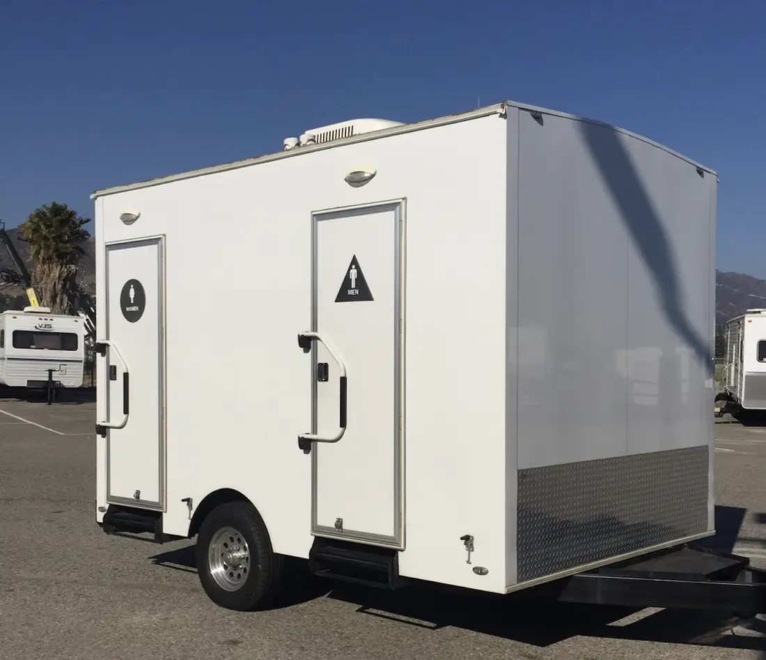 White restroom trailer with two separate exterior doors marked Men and Women, each with its own steps.
